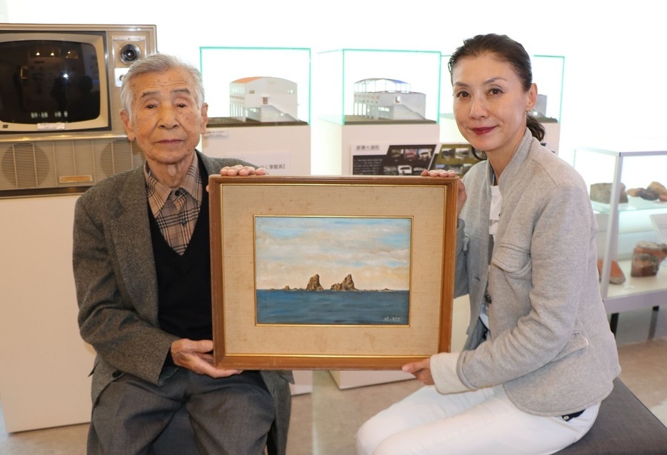 軍艦島デジタルミュージアムの久遠裕子さん（右）に三ツ瀬の風景画を手渡す加地さん＝２０２２年１１月、長崎市、軍艦島デジタルミュージアム