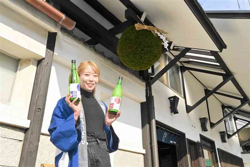 杉玉の前で新酒を手にする山村酒造の社員＝11日、高森町