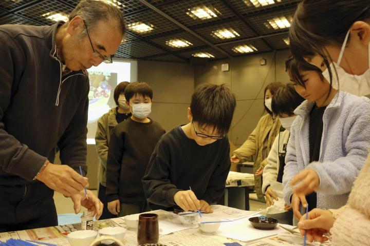 渡辺さん（左）に教わり、桜井漆器に絵を描く子どもたち