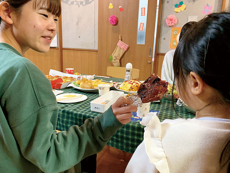 職員（左）からローストレッグを勧められ、頬張る施設利用者＝25日夜、熊谷市