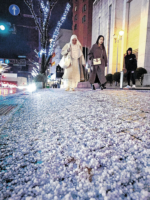 あられで歩道が白くなり、足元を気にしながら歩く人＝金沢市香林坊２丁目