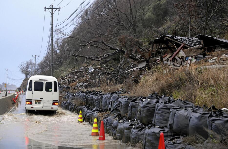 土砂崩れに巻き込まれ、土のうにとどめられたまま残る建物。道路は雨で冠水していた＝15日午後、石川県珠洲市