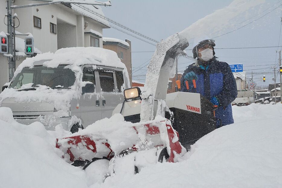 除雪機で歩道を除雪する男性。走る車の屋根には雪が残ったまま＝23日午前8時50分ごろ、弘前市紺屋町