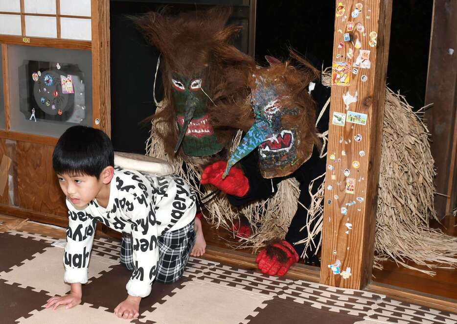 子どもの背中に褒美の年餅を乗せるトシドン＝３１日午後７時１０分、薩摩川内市下甑町手打