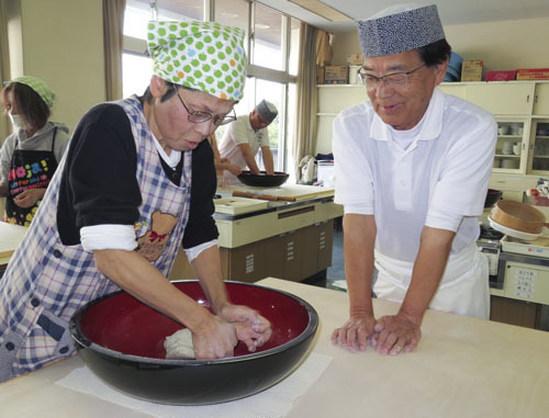 【講師の伊藤さん（右）の手ほどきでそばを打つ参加者＝伊勢市二見町の二見公民館で】