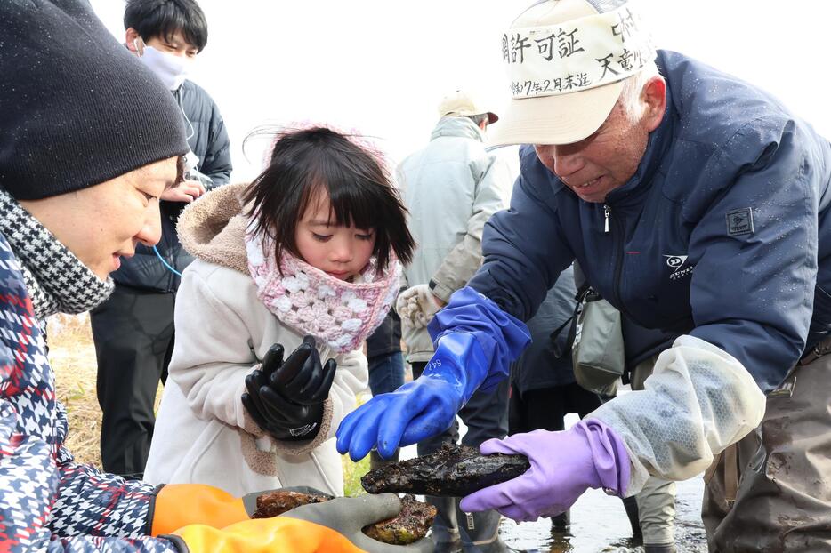 中村さん（右）から石の裏にいるざざ虫の解説を聞く参加者たち