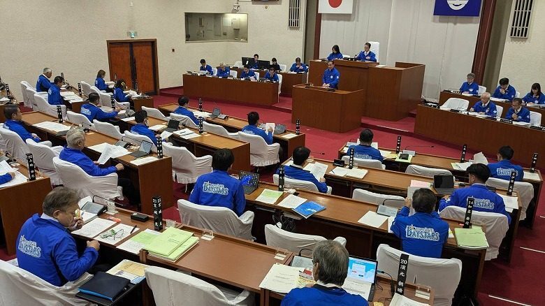 プロ野球横浜DeNAベイスターズの日本シリーズ制覇を記念し、球団名の入った青色のジャンパーを着用して本会議に臨む市議と職員ら＝5日、宜野湾市議会