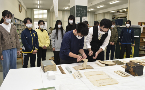 【桐田氏（手前右）の指導で鎌倉時代の写本に触れる生徒（同左）ら＝津市新町の県立津高図書館で】