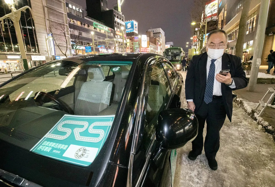 ライドシェアの標示をつけた車の横でスマホの画面を確認する運転手＝12日、札幌市中央区のススキノ（植村佳弘撮影）