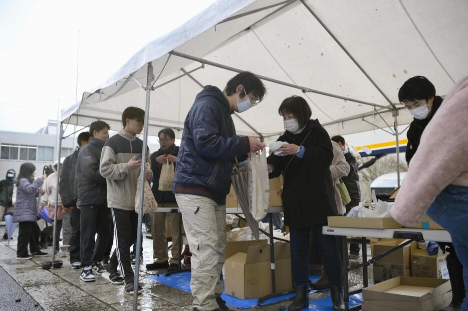 石川県輪島市の重蔵神社で、年越しそばなどが入った袋を受け取る人たち＝30日午後