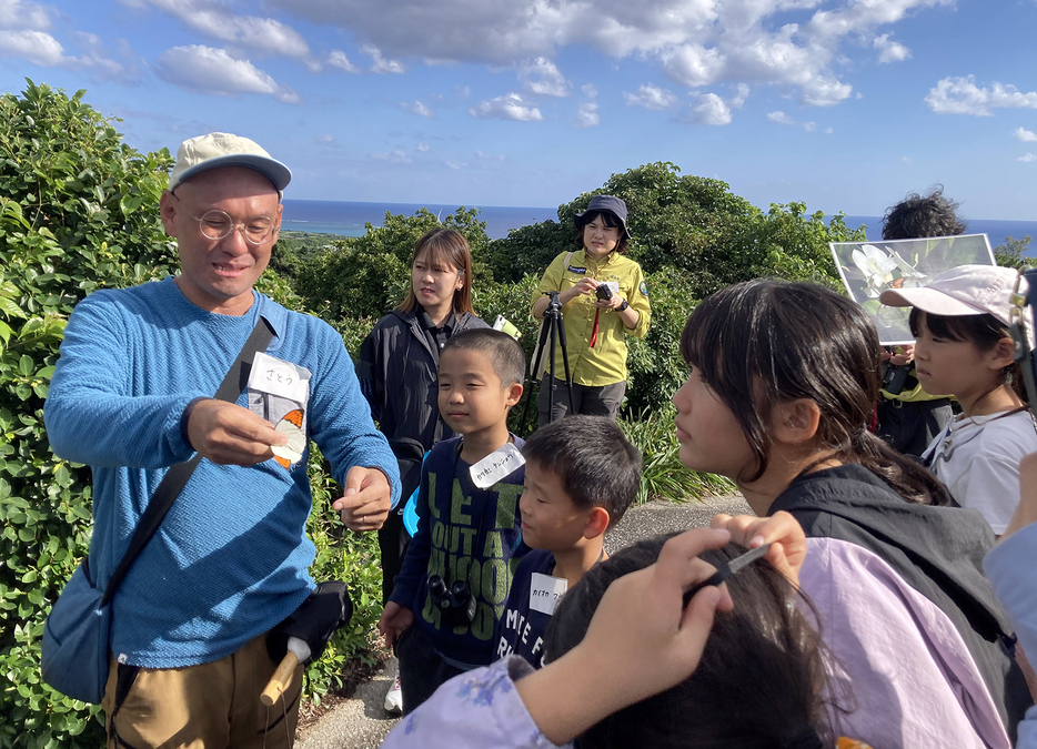 講師（左）が手に持つツマベニチョウをのぞき込む子どもたち＝11月30日、鹿児島県与論町