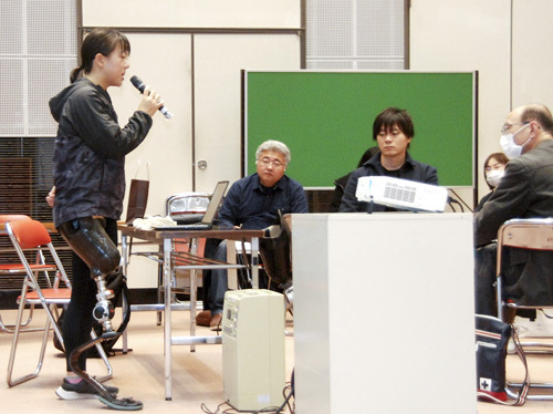 【分科会で競技用義足を装着し講演する保田さん（左端）＝亀山市東御幸町の市文化会館内中央コミュニティセンターで】