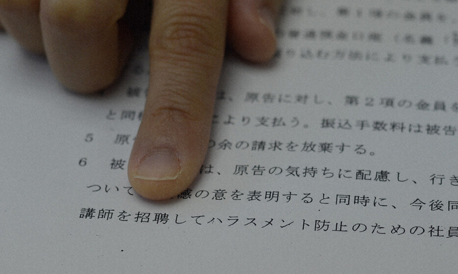 和解調書に記載された外部講師によるハラスメント防止の社員教育の条項を指さす原告女性＝長崎県諫早市で