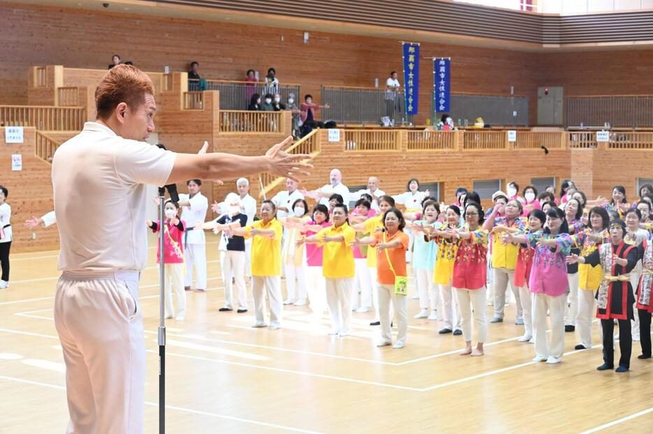 ラジオ体操をレクチャーするタレントのパッション屋良さん（左）と県女性連合会会員ら＝11月17日、豊見城市の沖縄空手会館