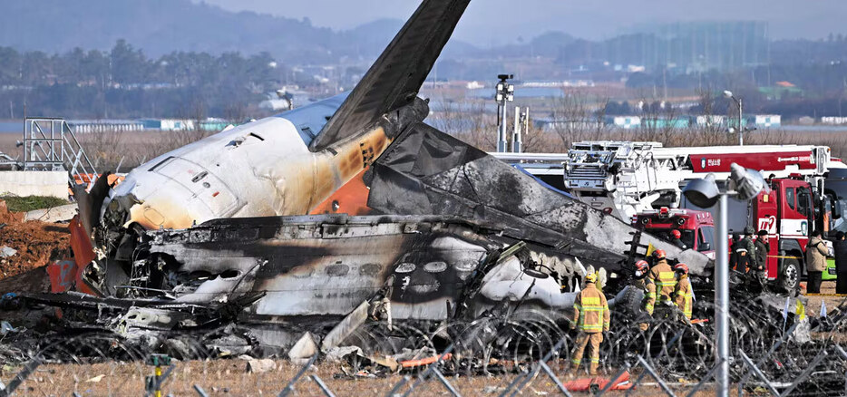 (写真：朝鮮日報日本語版) ▲181人が搭乗した旅客機は一瞬にして灰になった。29日午前9時3分ごろ、全羅南道の務安国際空港でタイ・バンコク発のチェジュ（済州）航空機が着陸の際、滑走路の外壁と衝突・爆発した。この事故で救助された生存者は2人だけで、残りの搭乗者は全員死亡した。写真は同日午後、燃えた旅客機の残骸を見る消防隊員たち。写真＝NEWSIS