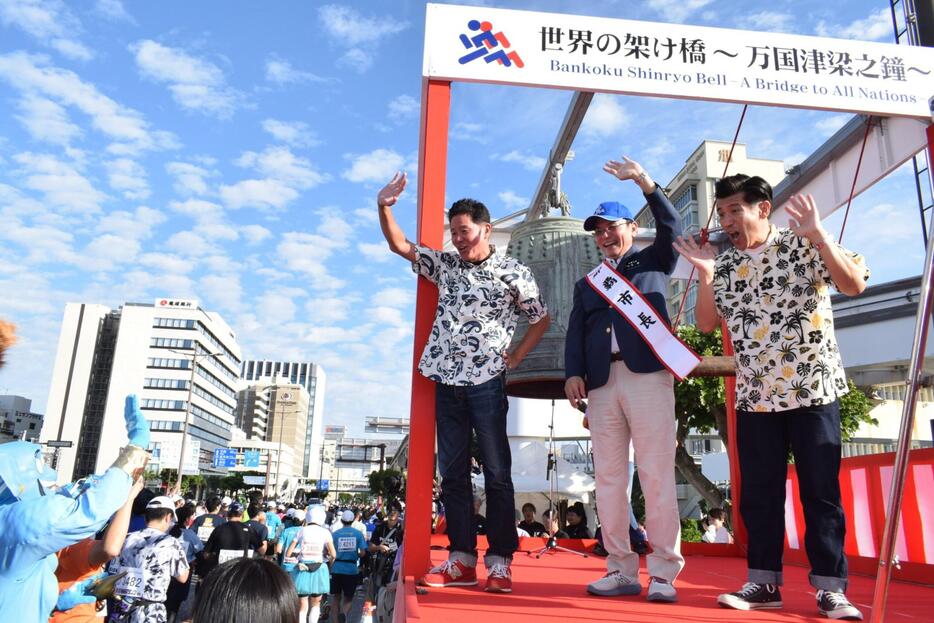 スタートの鐘を鳴らした後、ランナーに手を振る（左から）川田さん、知念覚那覇市長、ゴリさん＝那覇市の明治橋