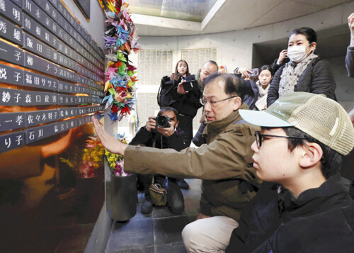 亡くなった姉と両親の銘板を取り付ける児玉さん（中央）（１４日、神戸市中央区の東遊園地で）＝代表撮影