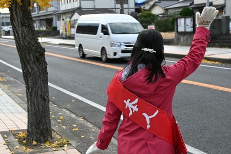 朝の通勤時間帯に行き交う車両に手を振る唐津市議選に立候補予定の新人＝唐津市西浜町