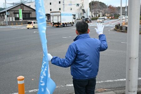 朝の通勤時間帯に行き交う車両に手を振る唐津市議選に立候補予定の新人＝唐津市町田