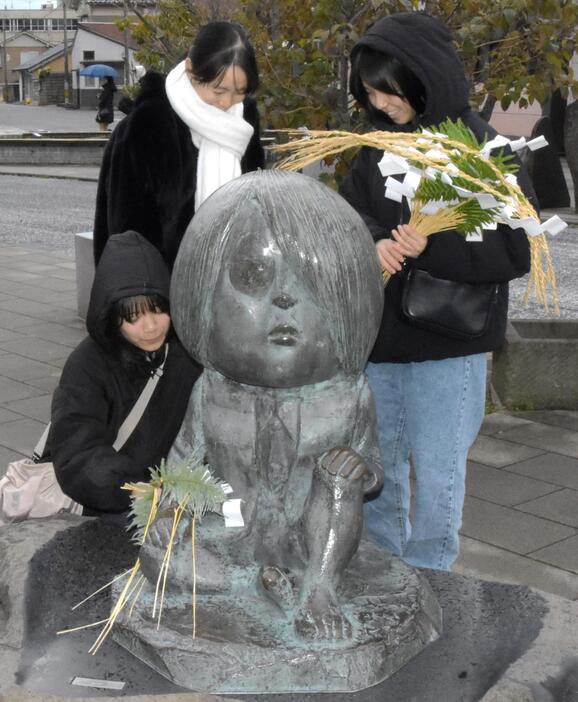 「水木しげるロード」にある鬼太郎のブロンズ像にしめ飾りを付ける人たち＝26日、鳥取県境港市