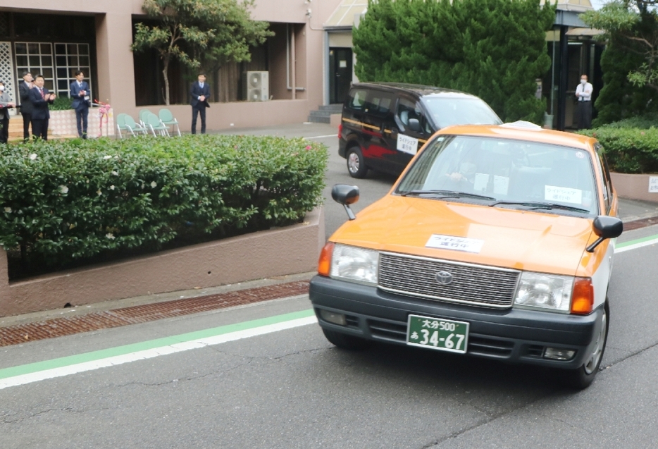 関係者に見送られながら出発する「日本版ライドシェア」の車両＝13日、別府市南立石