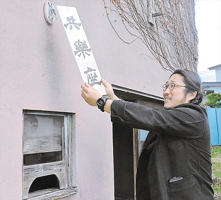 共楽座の入り口に新調した看板を掲げる渡辺さん。来年中の再オープンに向け、有志と準備を進めている