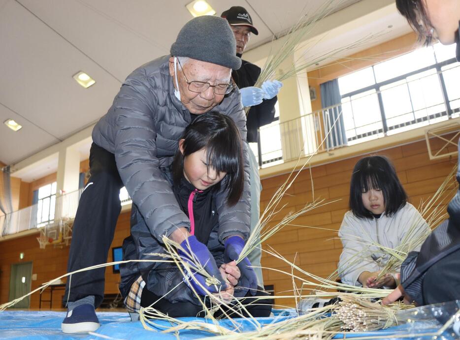 地元の老人クラブメンバーから指導を受け、しめ飾りを作る児童＝2024年12月19日午前8時52分、兵庫県丹波市春日町国領で