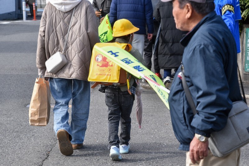 捜査車両などが行き来して騒然とする容疑者の自宅周辺で、地域住民らに見守られながら下校する児童＝北九州市小倉南区で2024年12月19日、成松秋穂撮影