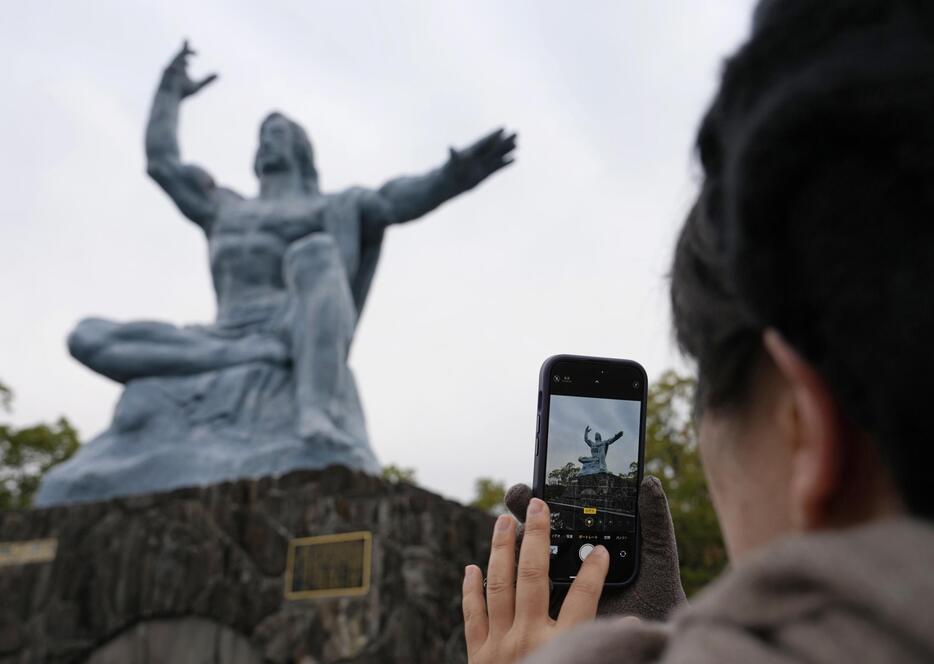 被団協へのノーベル平和賞授与から一夜が明け、長崎市の平和祈念像を撮影する女性＝11日朝