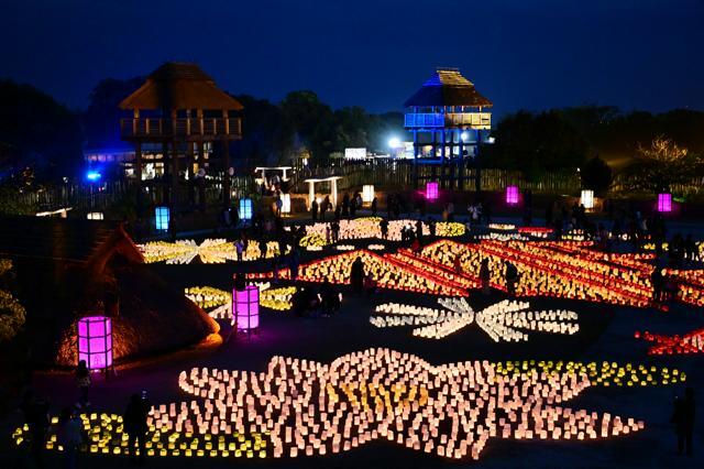 ともされたキャンドルの奥に、復元された弥生時代の建物群が浮かび上がった=2024年12月1日午後5時39分、佐賀県吉野ケ里町、日吉健吾撮影