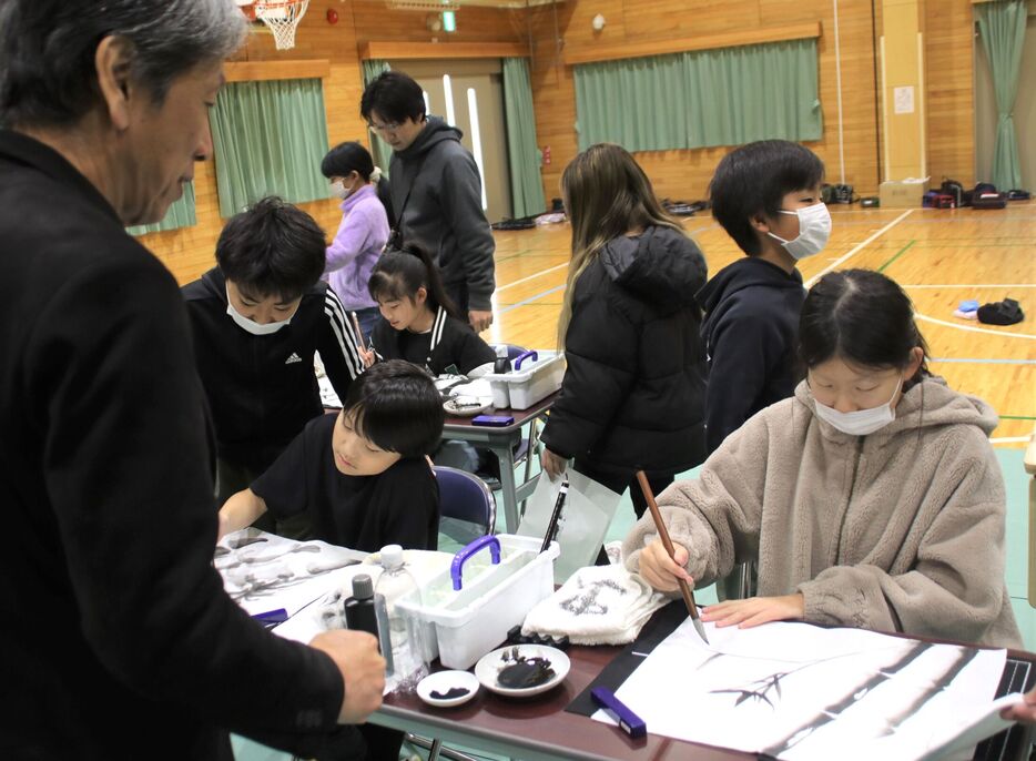 篠原さん（左）から水墨画の筆遣いを教わる児童（京都府南丹市八木町・八木東小）