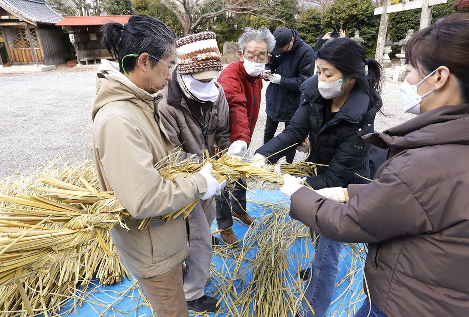 力を込めて3束をまとめてしめ縄に仕上げる氏子ら＝日野町の八雲神社で