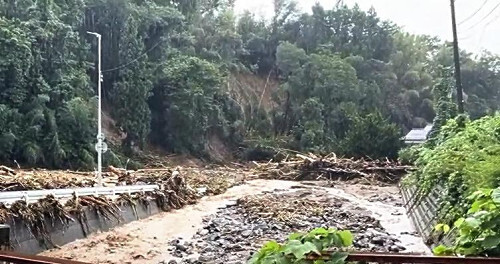 塚田川では、上流から流された大量の流木や土砂が橋（中央、奥）に詰まった。（近隣住民の提供動画から、９月２１日午後４時過ぎに撮影）