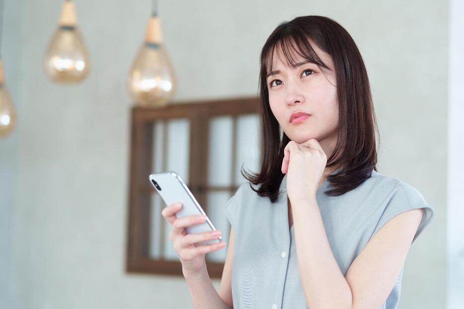 スマホを手に考える女性