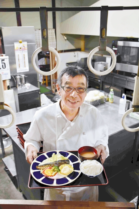 魚定食を手にする高田さん。店内にはつり革など鉄道関連のものがあふれる（香川県善通寺市で）