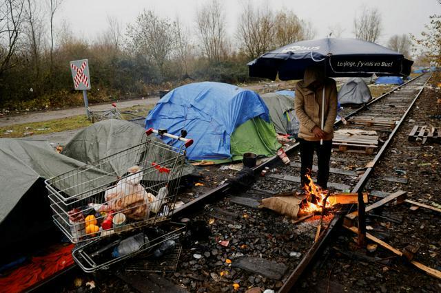 2021年12月4日、フランス・ダンケルク近郊のロオン海岸の仮設キャンプで、大雨が降る中、傘さすクルド人の難民申請者=ロイター