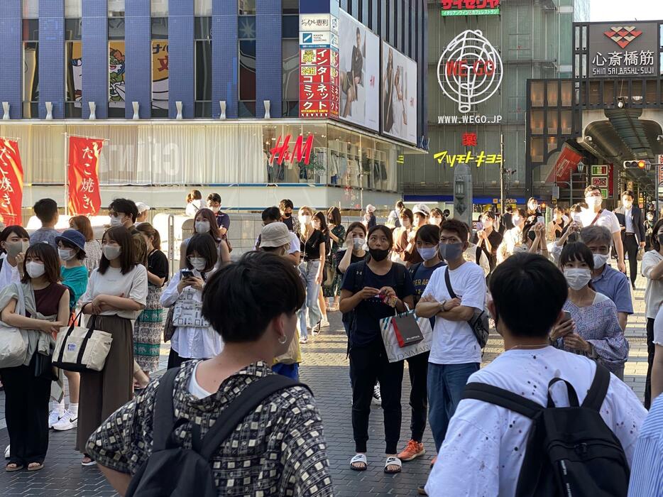 ［写真］大阪の戎橋では、通行人らが足を止めて会見中継を見つめていた＝27日午後5時10分ごろ、大阪市中央区で