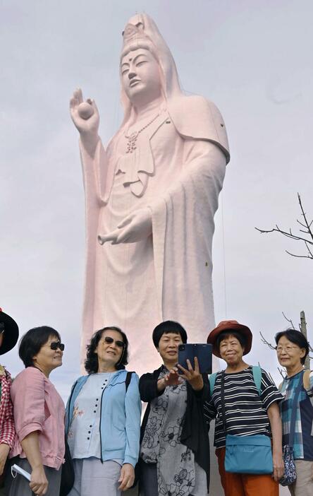 ピンク色の「仙台大観音」を背に写真を撮る外国人観光客＝25日午前、仙台市