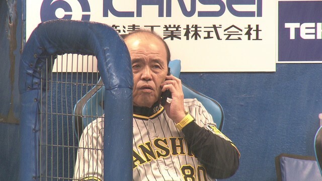 雨の中ベンチで電話をする阪神の岡田彰布監督