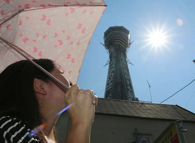 [写真]通天閣を見上げると強い日差しに思わず日傘をさす女性=14日午後3時ごろ、大阪市浪速区で（撮影：柳曽文隆）