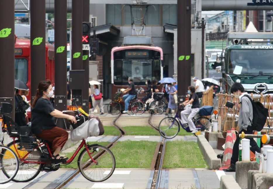 [写真]日傘や帽子にマスクという姿の人が行き交う。チンチン電車の運転士やトラックの運転手もマスクを着けている＝22日午前11時半ごろ、大阪市阿倍野区で