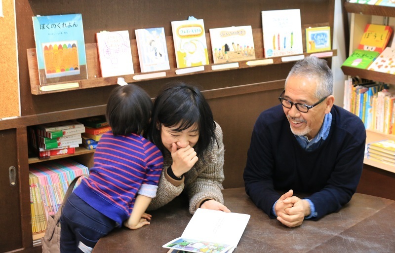 [写真]店を訪れていた親子と楽しく会話しながら読書。丸太のテーブルや切り株のイス、そして本棚まですべて増田さんの手作り