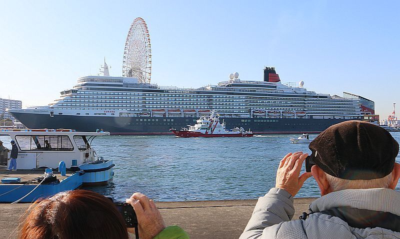 [写真]夢中でシャッターを切る見物人（手前）。日本最大級の観覧車もクイーン・エリザベスと並ぶと小さくみえる？手前は大阪市の消防艇と渡船=22日午前8時ごろ、大阪市此花区から同港区の大阪港を撮影